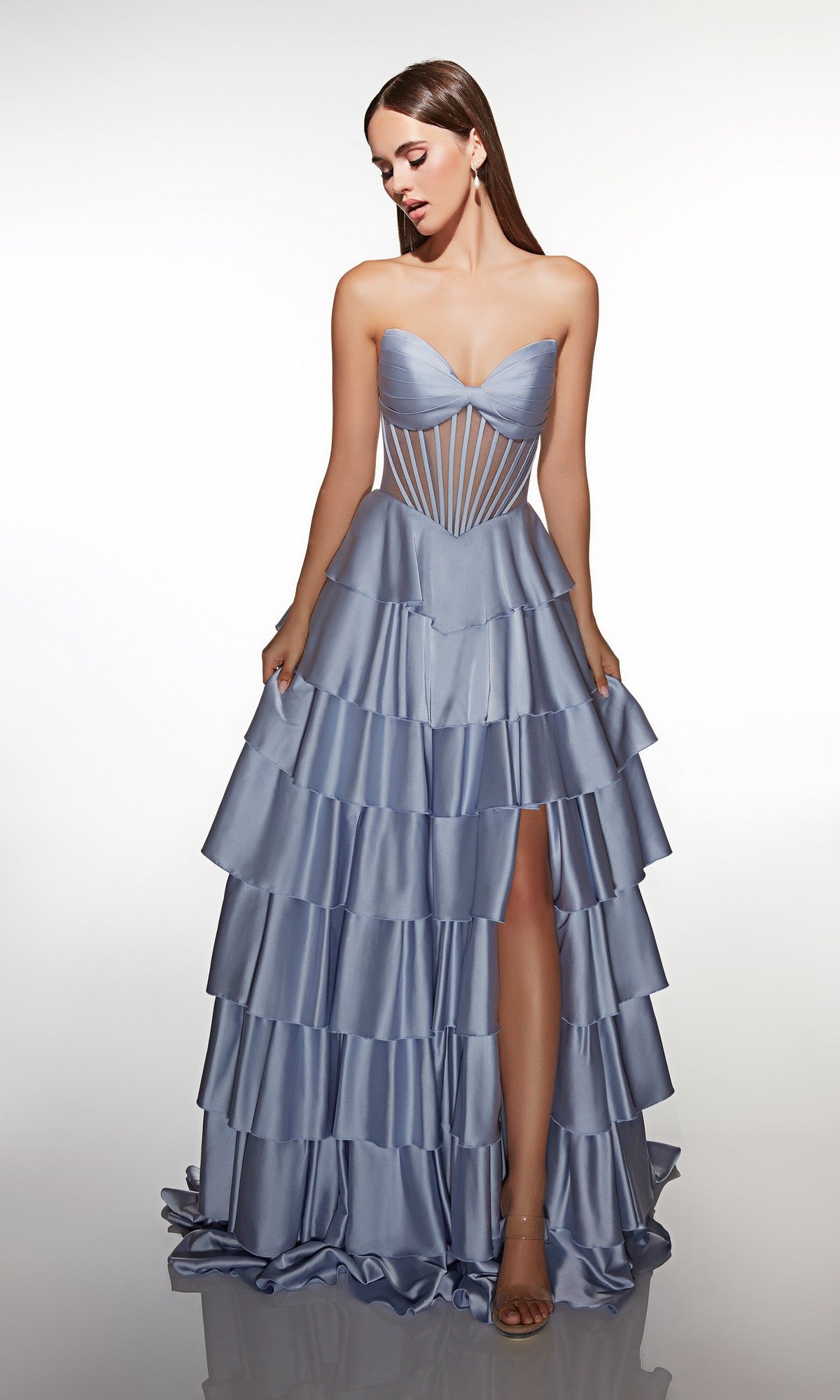 A woman wears the Alyce 62056 long prom dress in French Blue, featuring a strapless satin sweetheart neckline, corset-style bodice, and tiered ruffle A-line skirt with a high slit, standing against a plain white background.